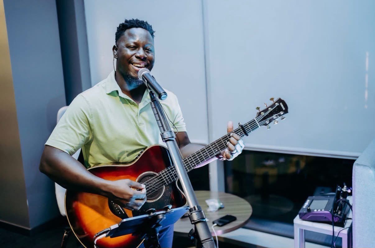 Joel Kisakye singing and playing acoustic guitar at a live event