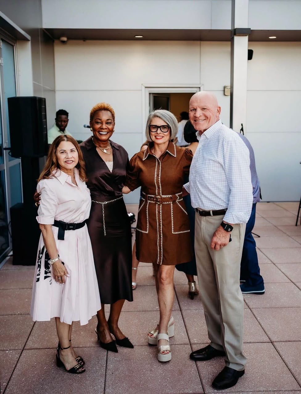 Four smiling guests posing together on a rooftop terrace during an event