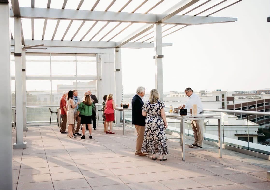 Guests gathered under a pergola on a rooftop terrace in the evening light